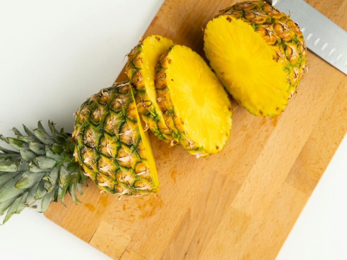 Ananas mit abgeschnittener Krone und Scheiben auf einem Holzbrett