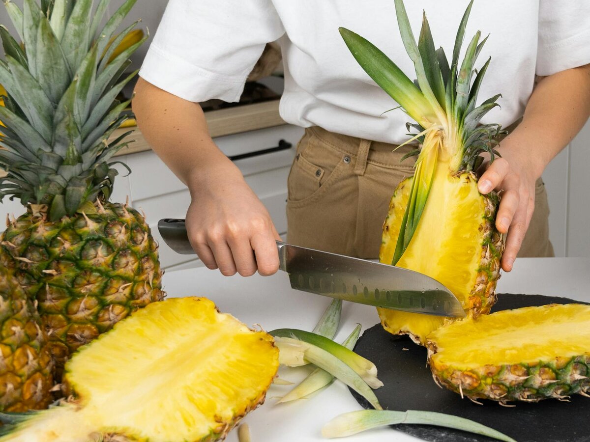 Eine Ananas wird mit einem Messer von Hand geschnitten